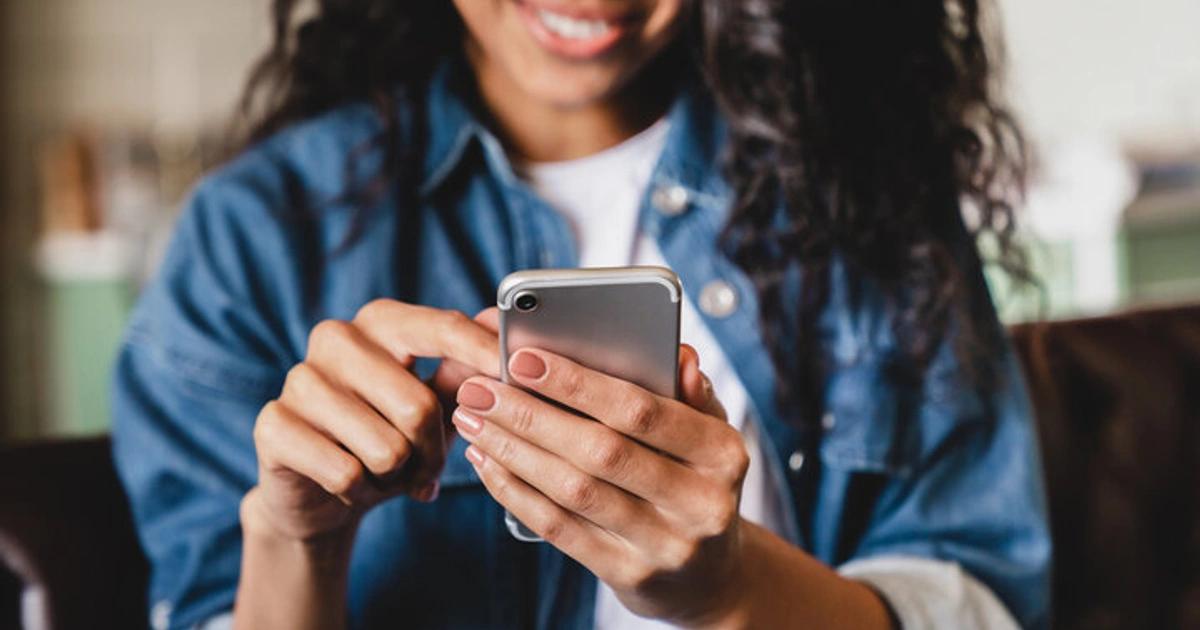 Cropped shot of an african-american young woman using smart phone at home. Smiling african american woman using smartphone at home, messaging or browsing social networks while relaxing on couch